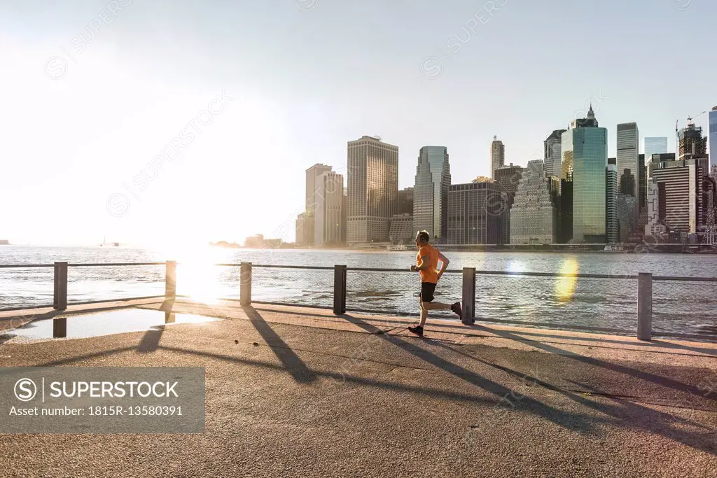USA, Brooklyn, man jogging in front of Manhattan skyline in the evening