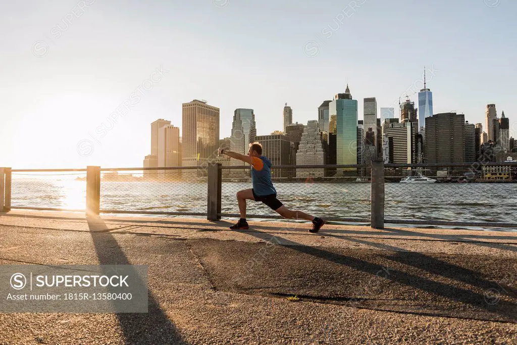 USA, Brooklyn, man doing stretching exercises in front of Manhattan skyline in the evening