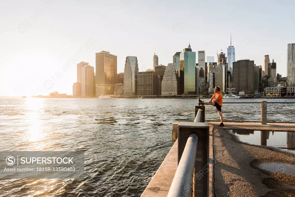 USA, Brooklyn, man doing stretching exercises in front of Manhattan skyline in the evening