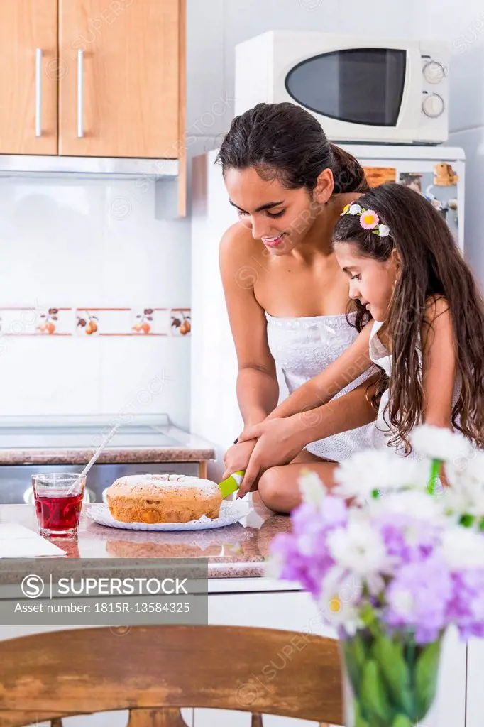 Teenage girl and her little sister in kitchen cutting a cake