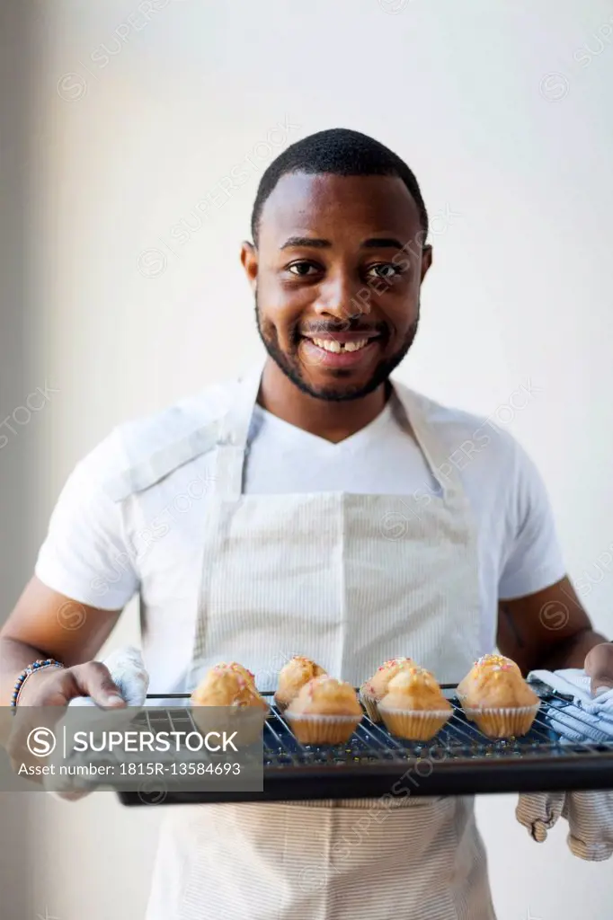 Happy young man holding tray with muffins