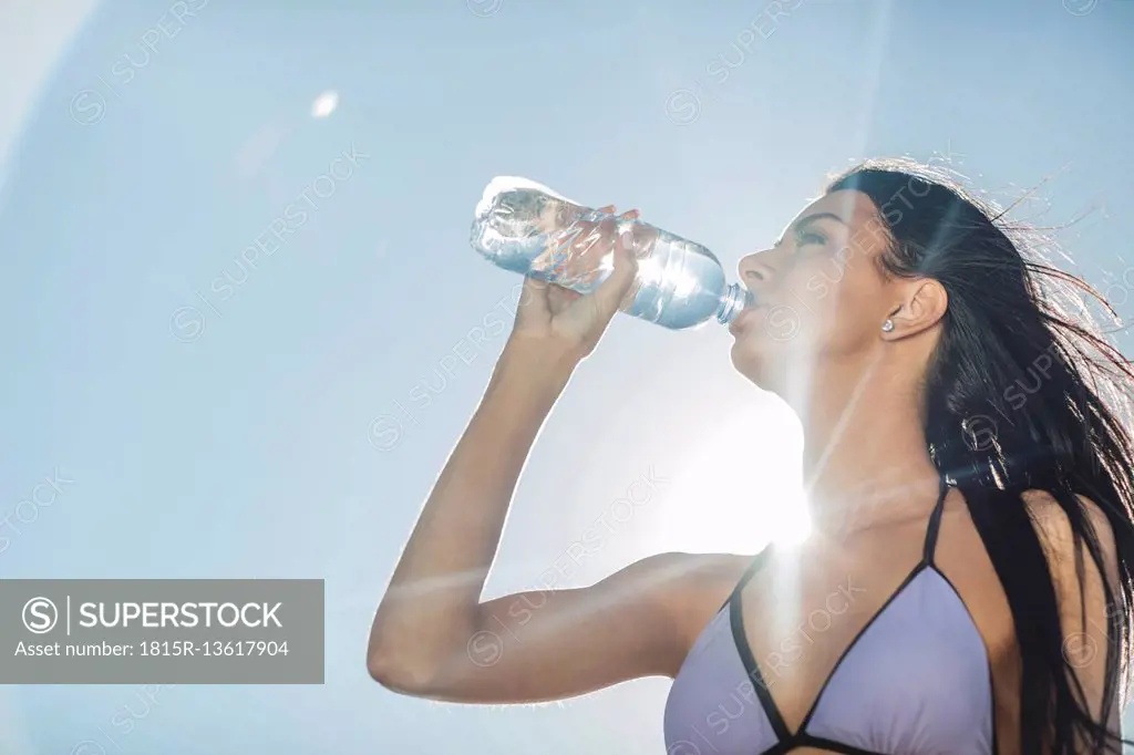 Young woman in bikini drinking water from bottle