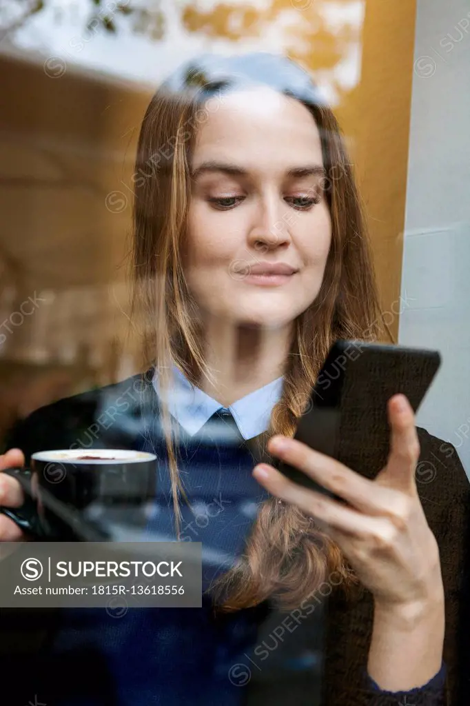Smiling young woman in coffee shop with cup of coffee looking at smartphone