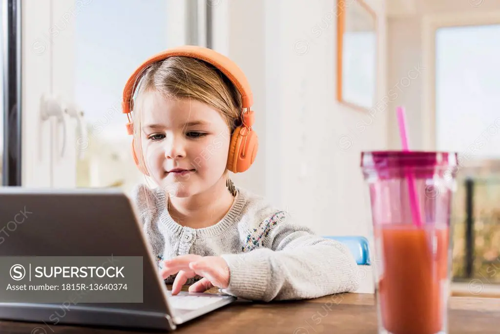 Little girl sitting at home using laptop and headphones