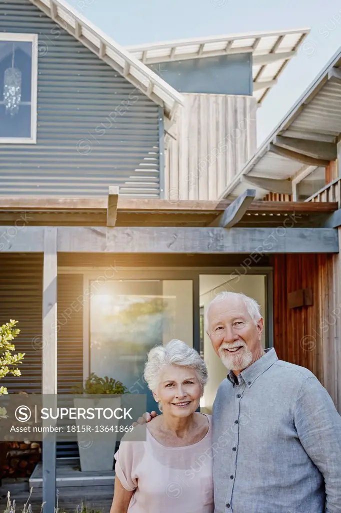 Senior couple standing in front of their house, looking confident