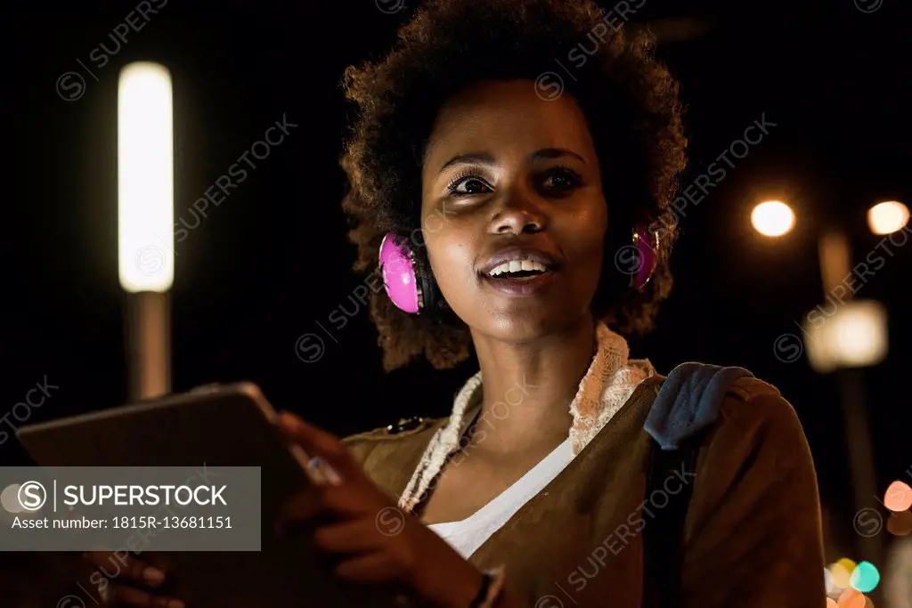 Portrait of young woman with headphones and tablet by night