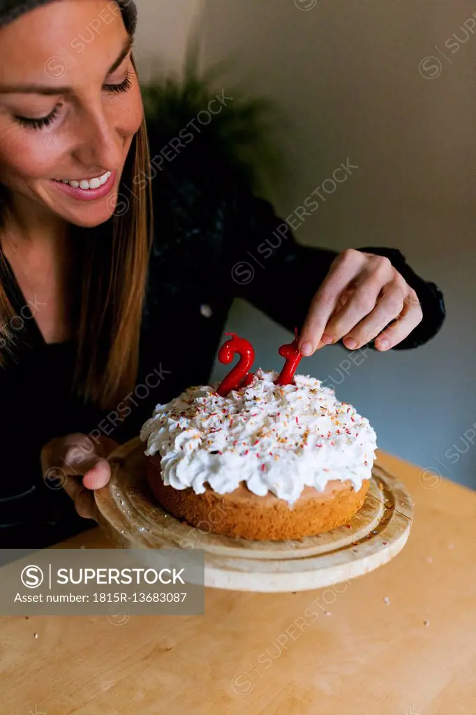 Young woman decorating birthday cake with red candles