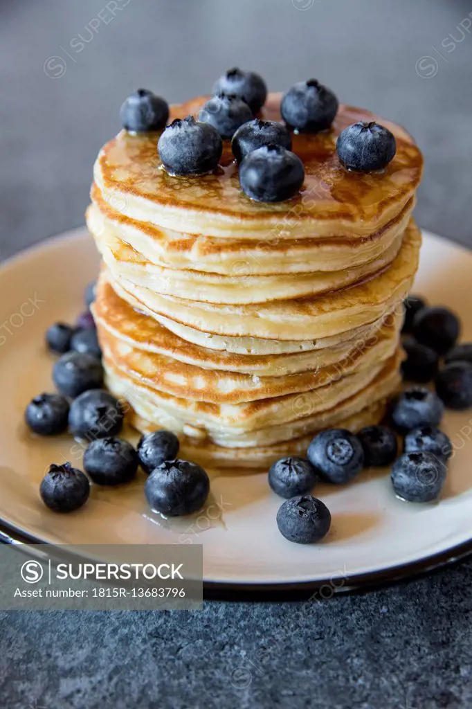 Dish with pile of pancakes and blueberries with maple sirup