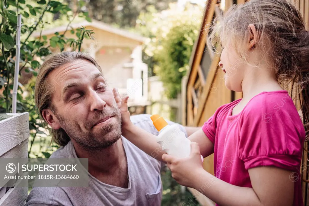 Daughter applying sunscreen on father's face in garden