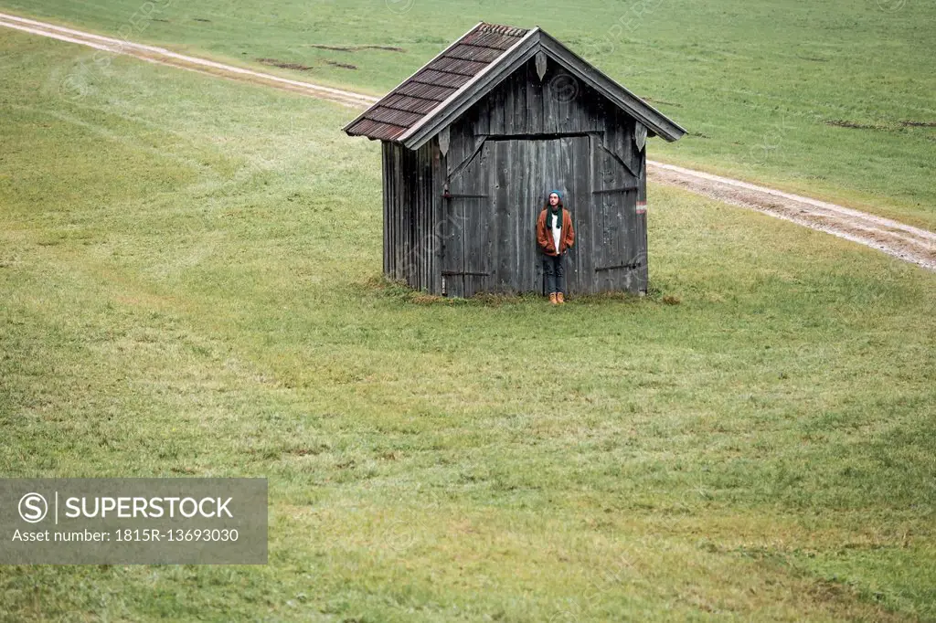 Young man standing in front of wooden hut on a meadow