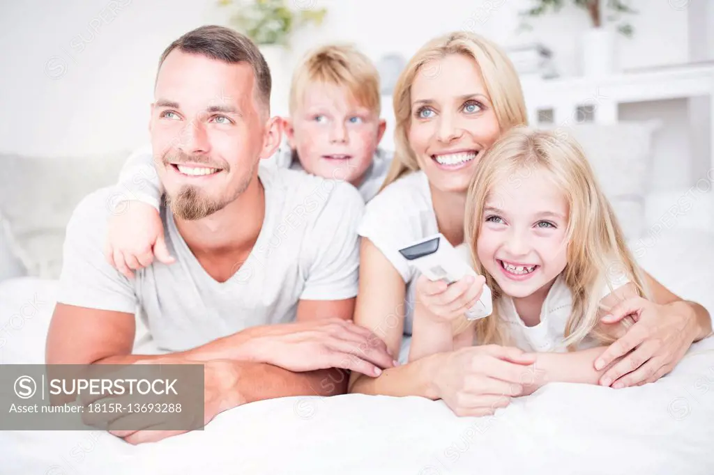 Happy family lying in bed watching Tv
