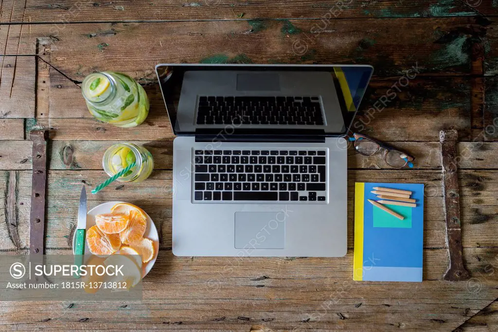 Glass bottle of infused water, notepad, spectacles, laptop, peeled tangerine