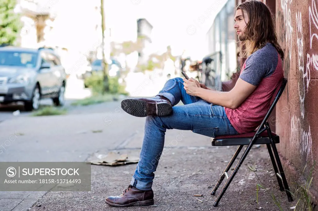 USA, New York City, man sitting on a chair using cell phone in Williamsburg, Brooklyn