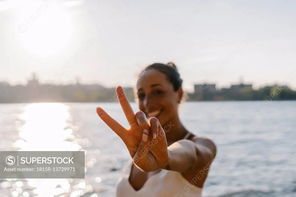 Young woman in Brooklyn standing at East River giving victory sign