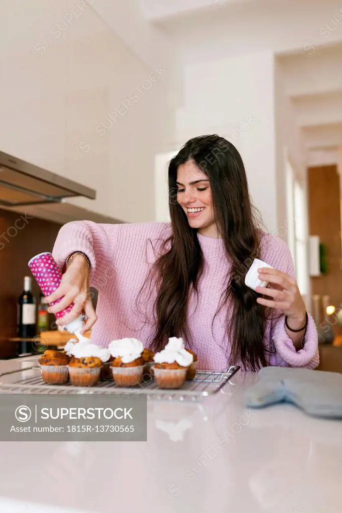 Young woman topping cup cakes with whipped cream