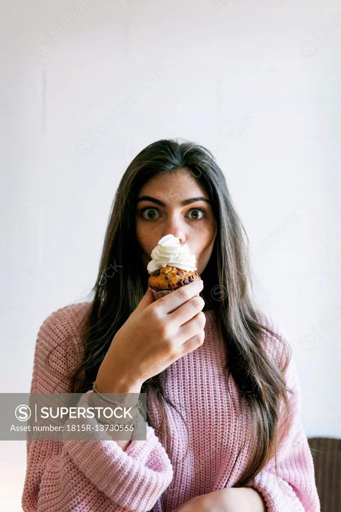 Young woman eating a cup cake with whipped cream