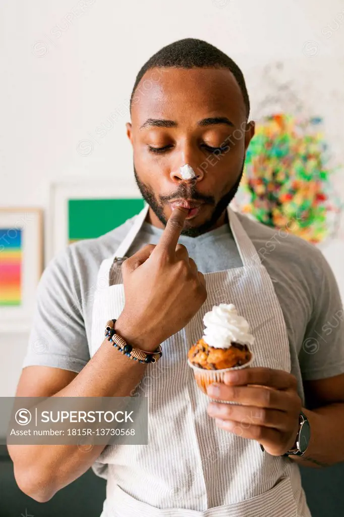Young man eating a cup cake with whipped cream, licking finger