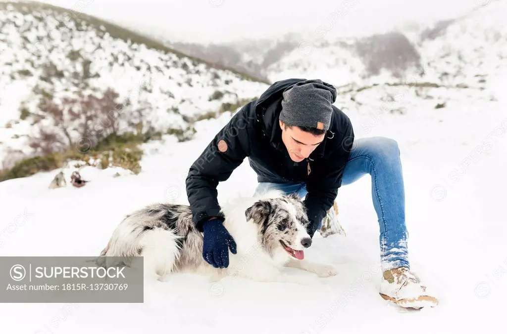 Young man stroking his dog in the snow