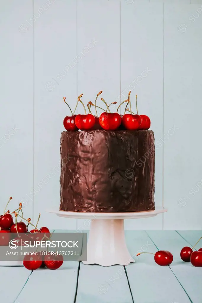 Cake with chocolate icing and cherries on top on cake stand