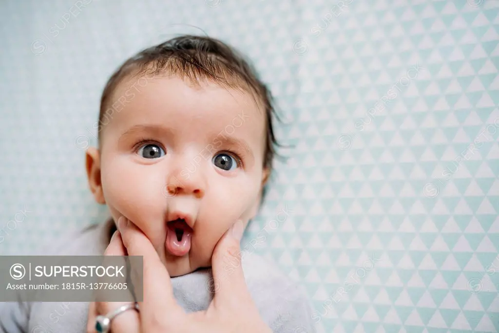Baby with funny face, mother's Hand pressing her cheek
