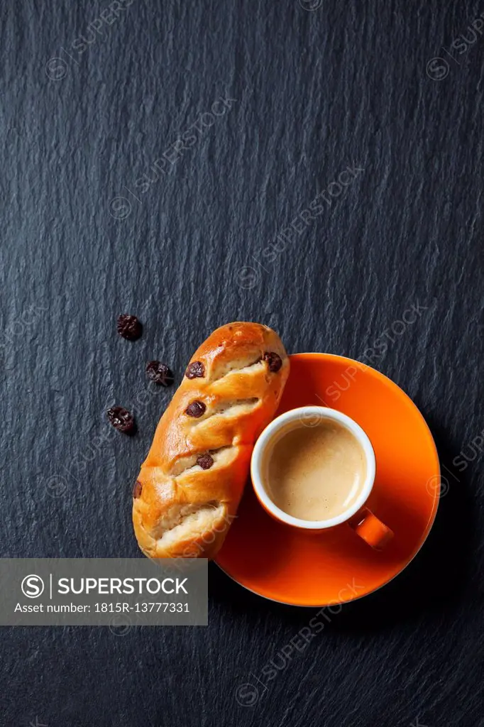 Chocolate bun with raisins and cup of espresso on slate