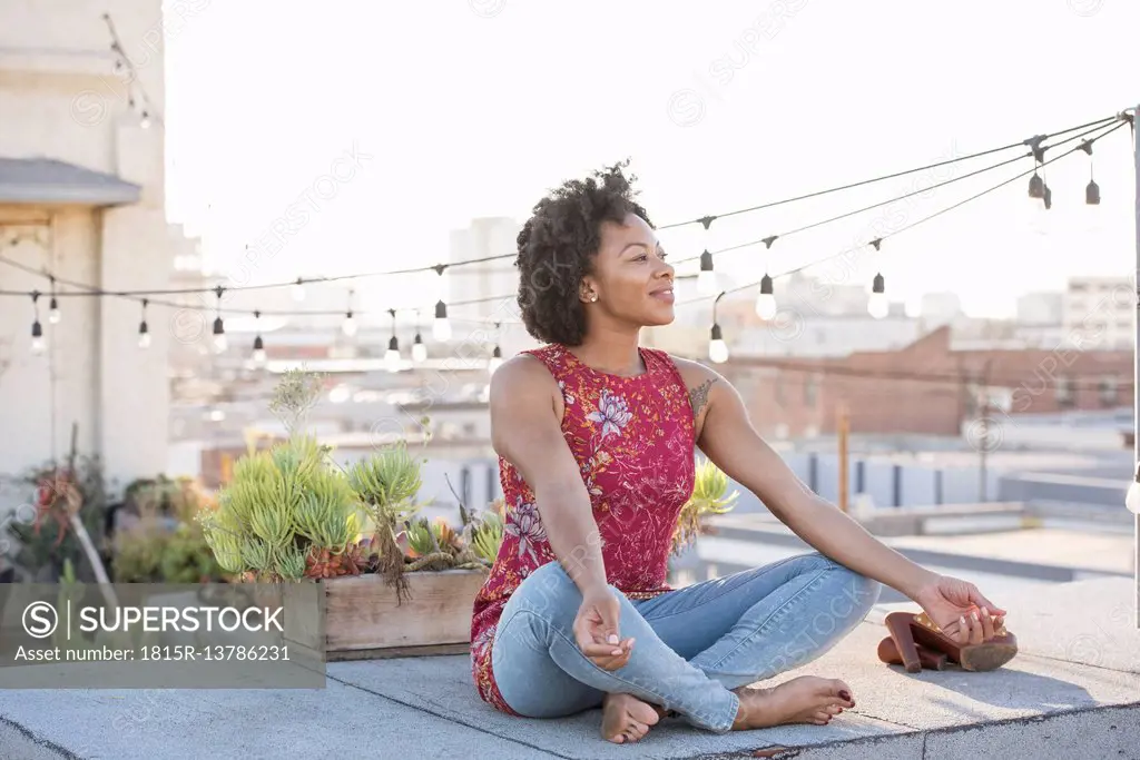 Young woman sitting on rooftop terrace, enjoying the sun
