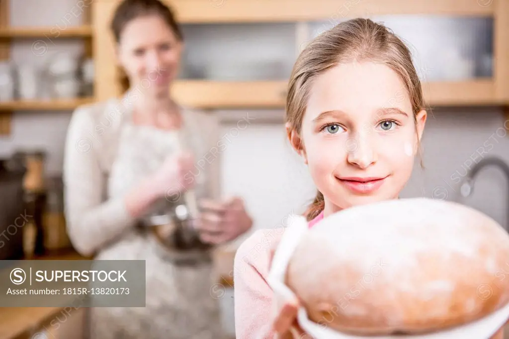 Girl holding bread in kitchen with mother in background