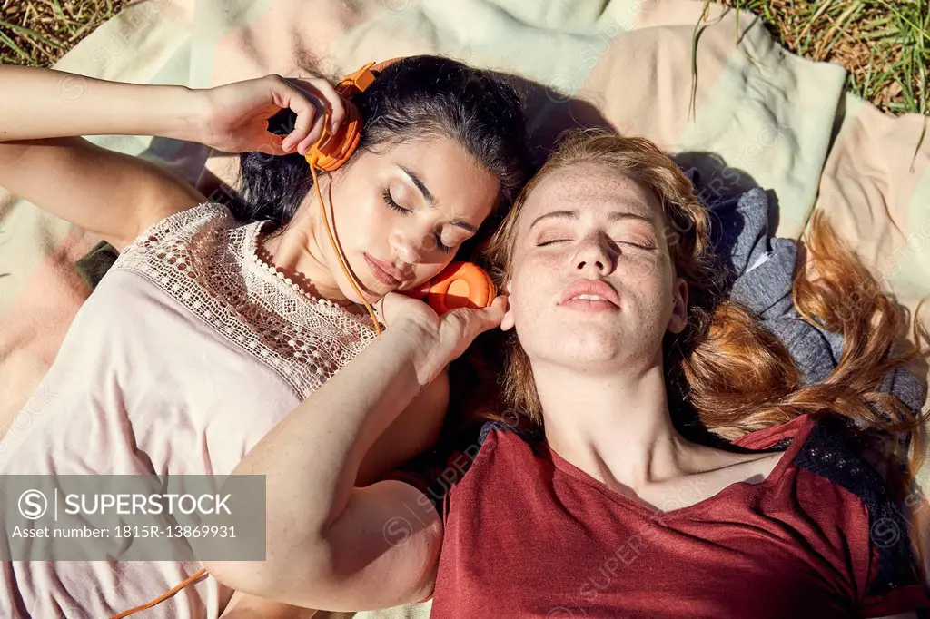 Portrait of two young women lying side by side on blanket listening music with headphones