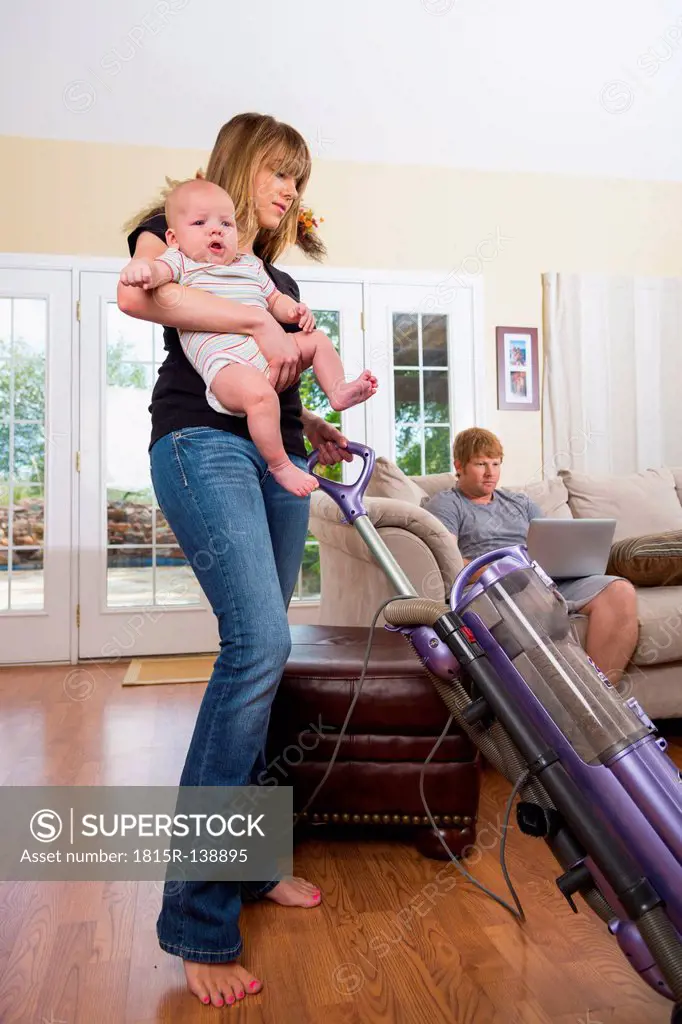 Mother with son using vacuum cleaner while father in background