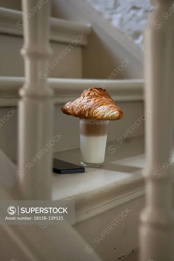 Croissant and drink on steps with mobile phone
