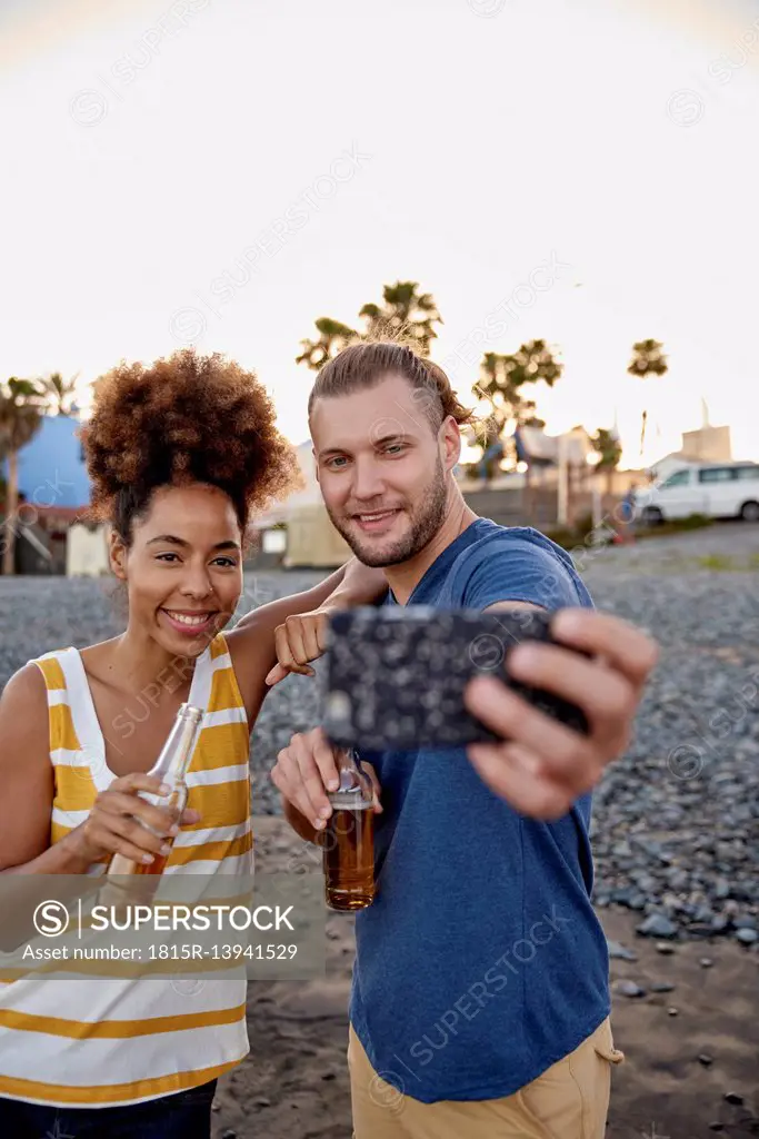 Two friends with beer bottles taking selfie on the beach