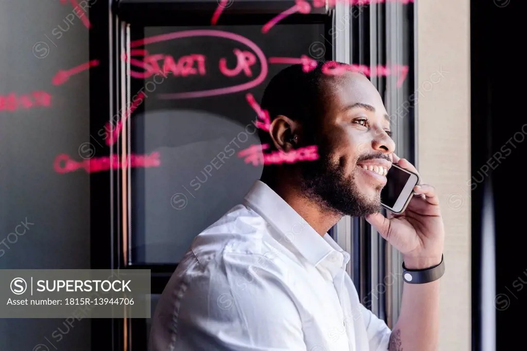 Smiling businessman on cell phone in office with writing on windowpane