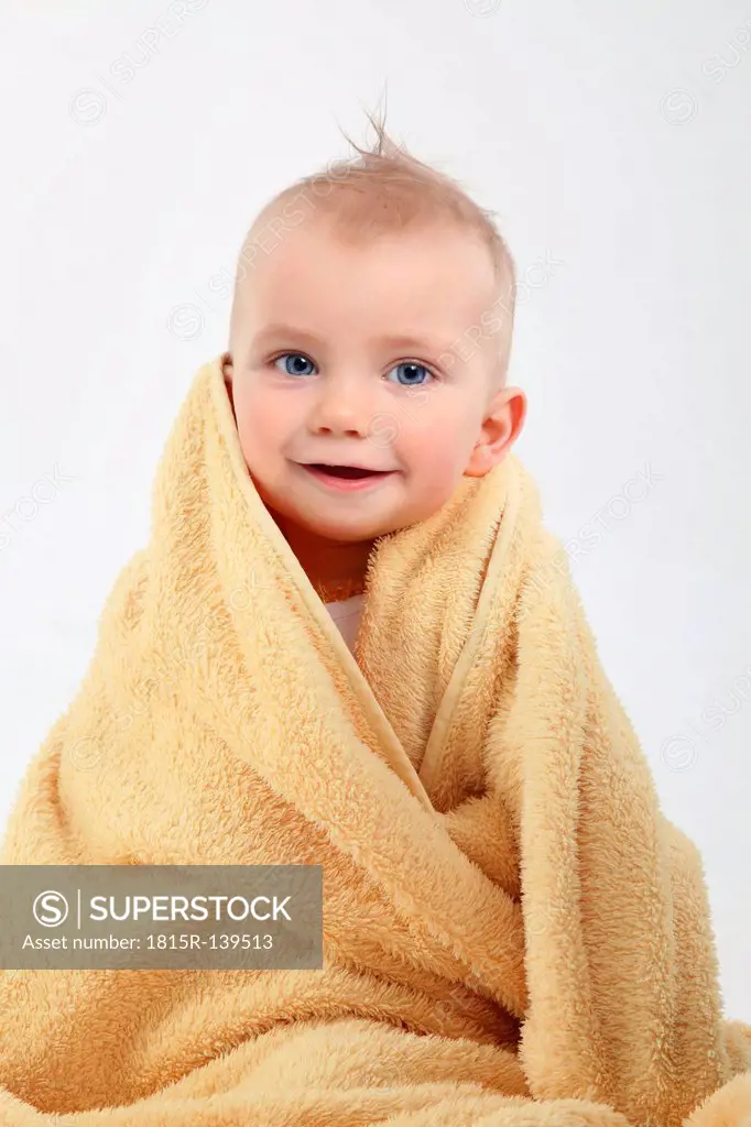 Portrait of baby boy wrapped in yellow towel, smiling