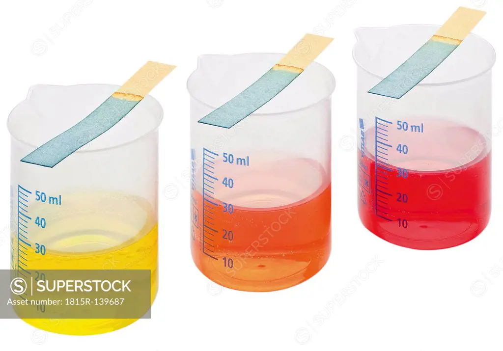 Meauring cylinders with coloured liquid and test strips on white background, close up