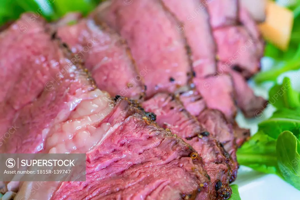 Sliced rib eye steak garnished with arugula and cantaloupe on plate, close up