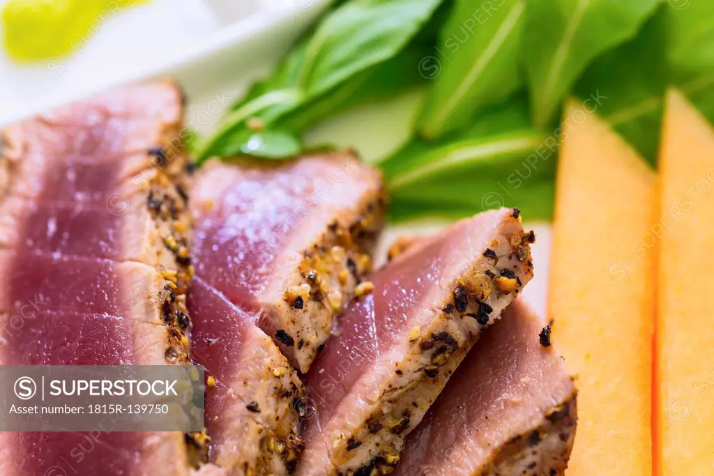 Slices of tuna steak with soy sauce, wasabi, arugula and cantalope on plate, close up