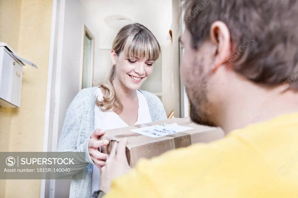 Germany, North Rhine Westphalia, Cologne, Young woman taking pizza box from delivery man, smiling