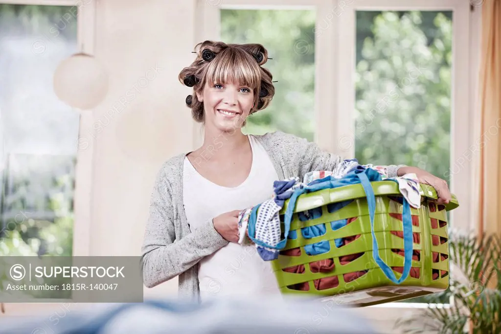 Germany, North Rhine Westphalia, Cologne, Portrait of young woman holding laundry basket, smiling