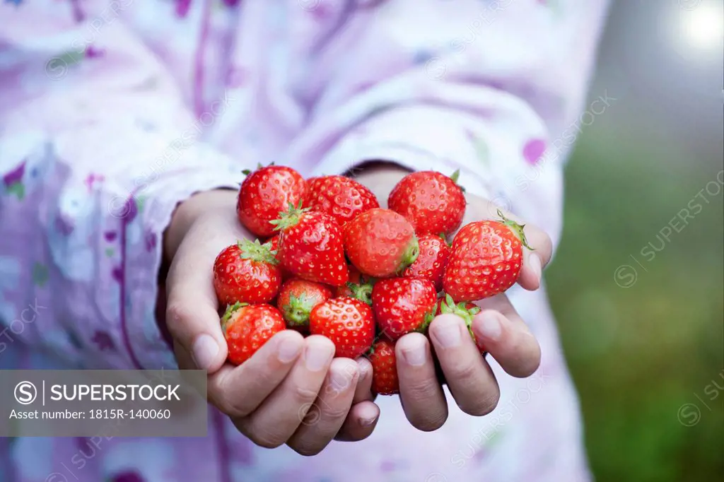 Germany, North Rhine Westphalia, Cologne, Girl holding strawberries in hands, close up