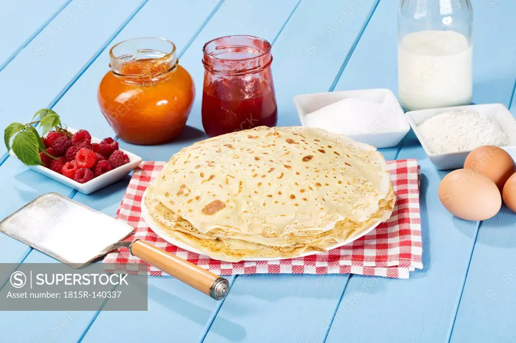 Pancakes with jam, raspberries, eggs, milk, sugar and flour on table
