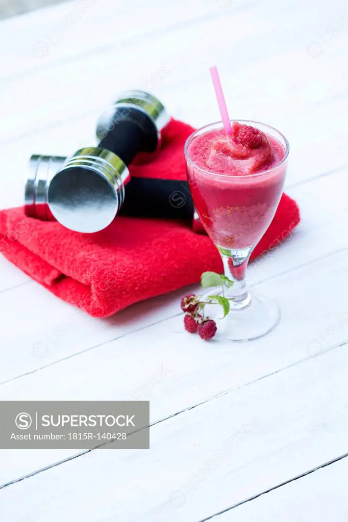 Raspberry smoothie with dumbbells and towel on table, close up