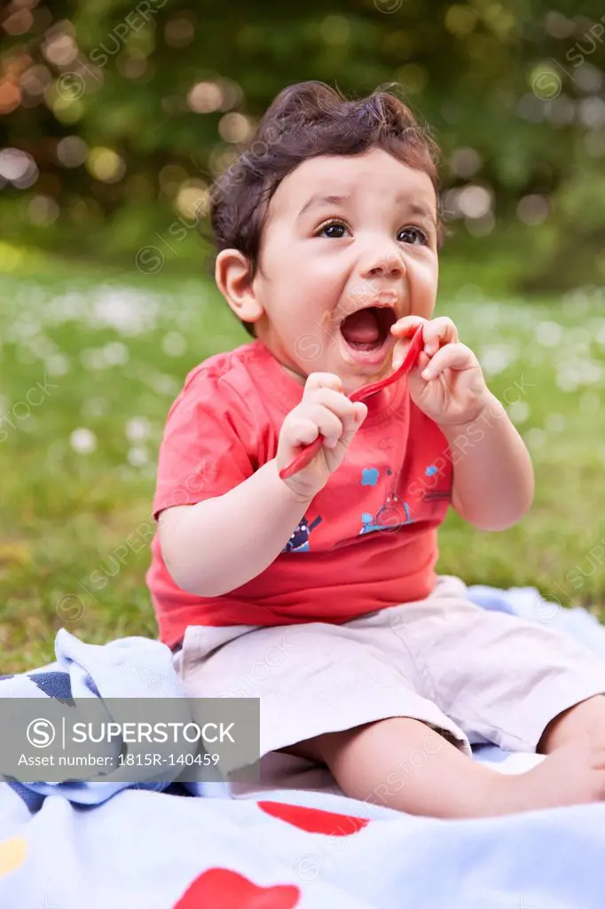 Baby boy holding spoon, looking up