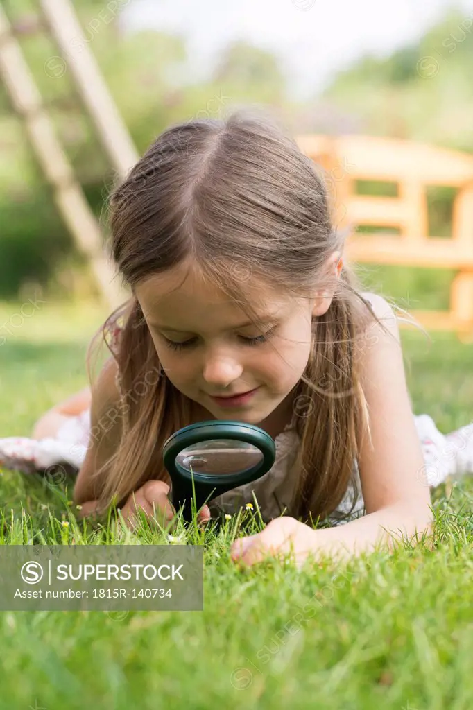 Germany, Bavaria, Girl looking through magnifying glass in graden