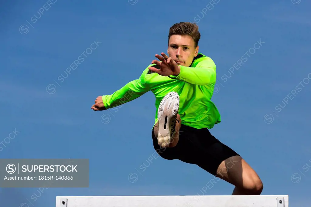 Germany, Man athlete jumping Hurdles on track