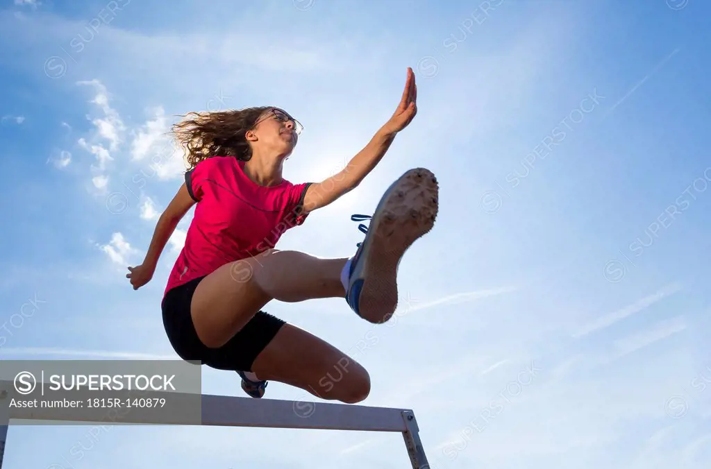 Germany, Young woman athlete jumping hurdles on track