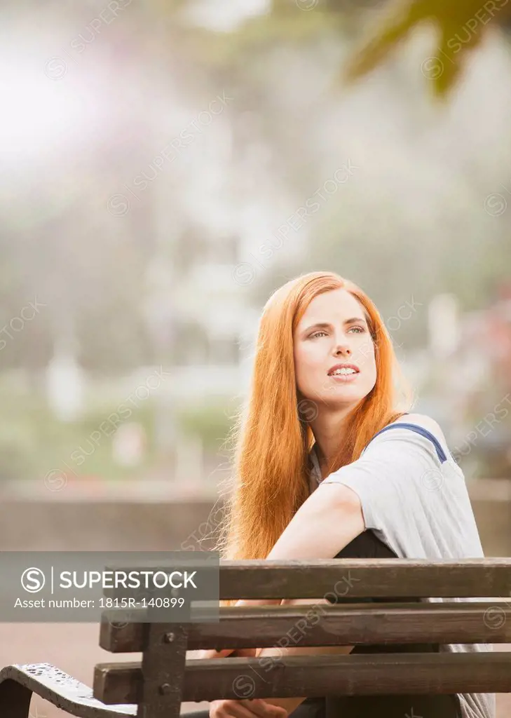 Germany, Berlin,Young woman sitting on bench and looking away