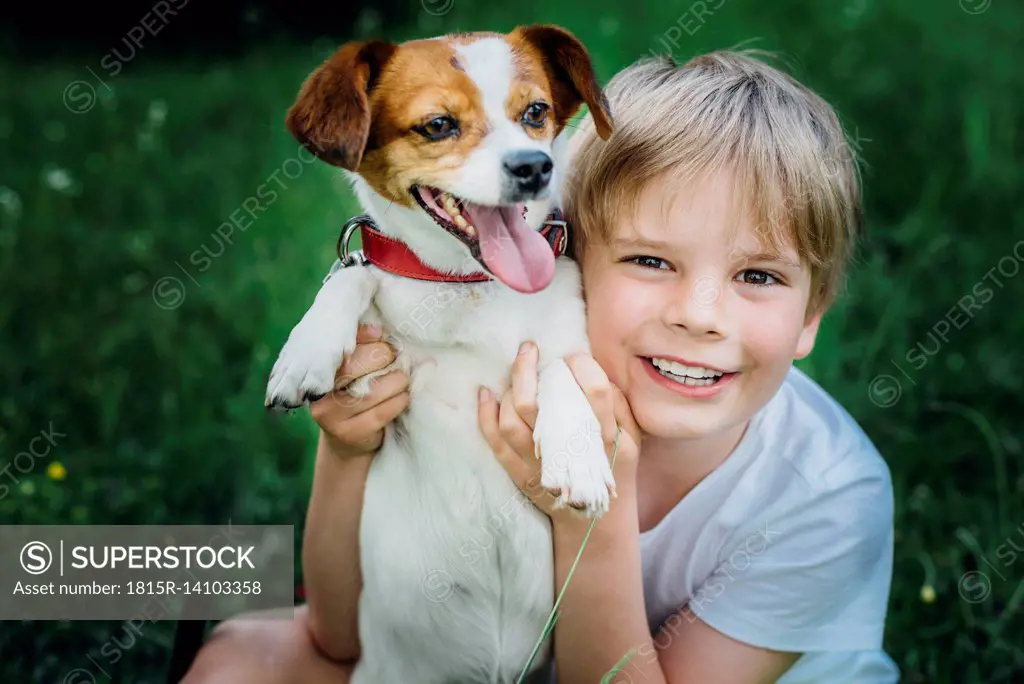Portrait of happy little boy with his dog on meadow in the garden