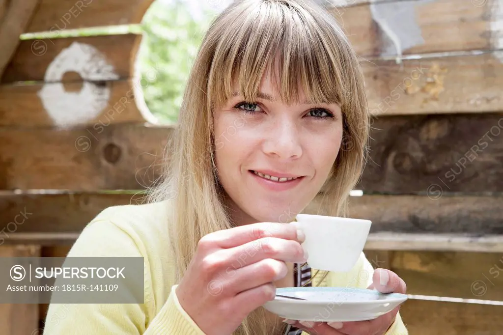 Germany, North Rhine Westphalia, Cologne, Portrait of young woman holding cup, smiling