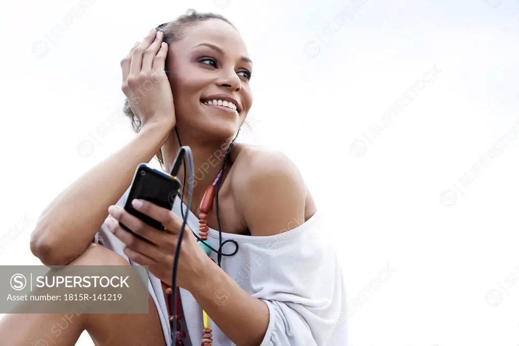 Germany, Young woman listening music with head phones, smiling