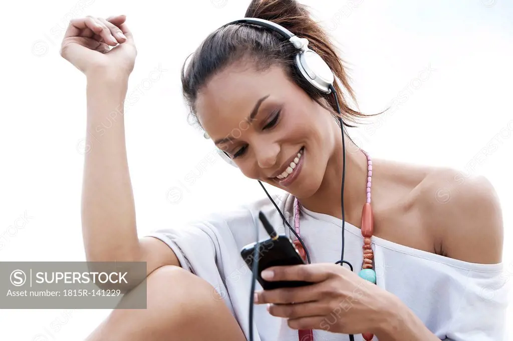 Germany, Young woman listening music with head phones, smiling